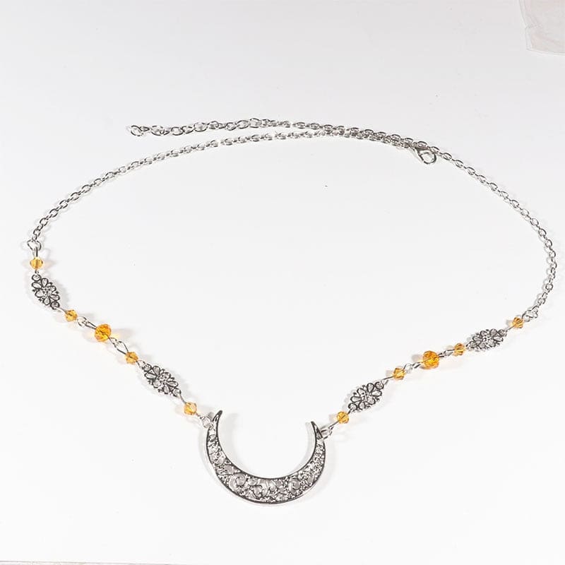 Silver-tone ornate crescent headdress with small amber-coloured beads and delicate ornamental links, arranged in an oval on a pale background with the clasp and chain visible.