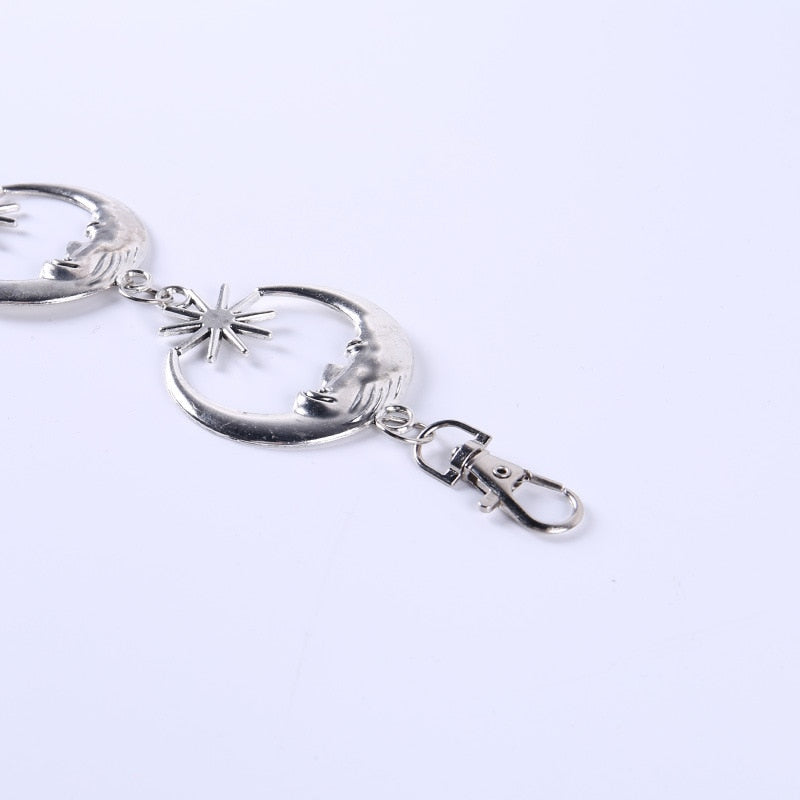 Close-up of a sculpted silver-tone crescent moon face, a pointed star and the belt's clip fastening on white.