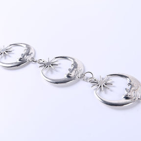 Linked silver-tone crescent moon faces and star shapes photographed diagonally on a pale background.