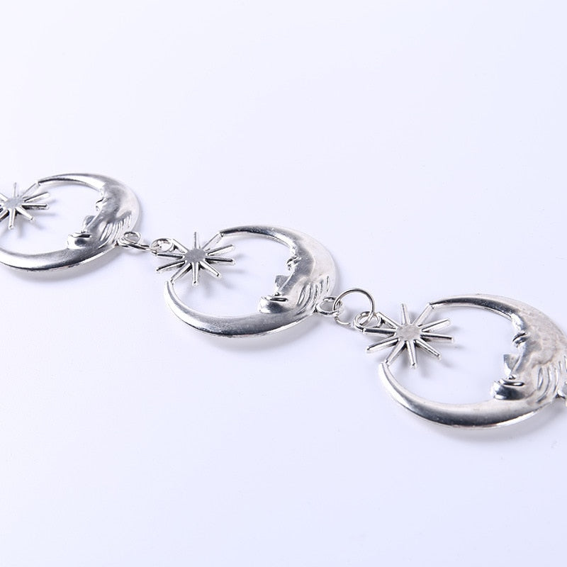 Linked silver-tone crescent moon faces and star shapes photographed diagonally on a pale background.
