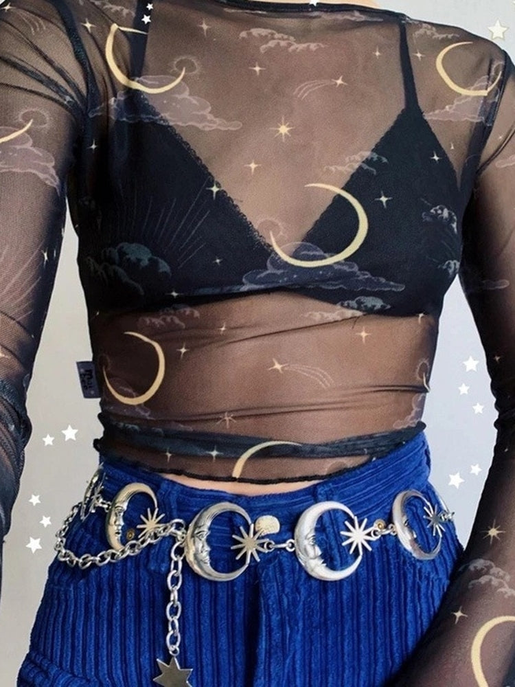 Silver-tone moon and star chain belt worn with blue corduroy trousers and a sheer celestial-print top, with a loose chain hanging at the front.