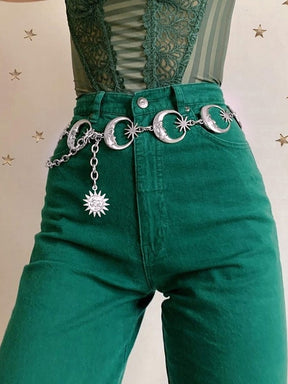 Silver-tone crescent moon belt around green high-waisted trousers, with a starburst charm hanging from the side chain.