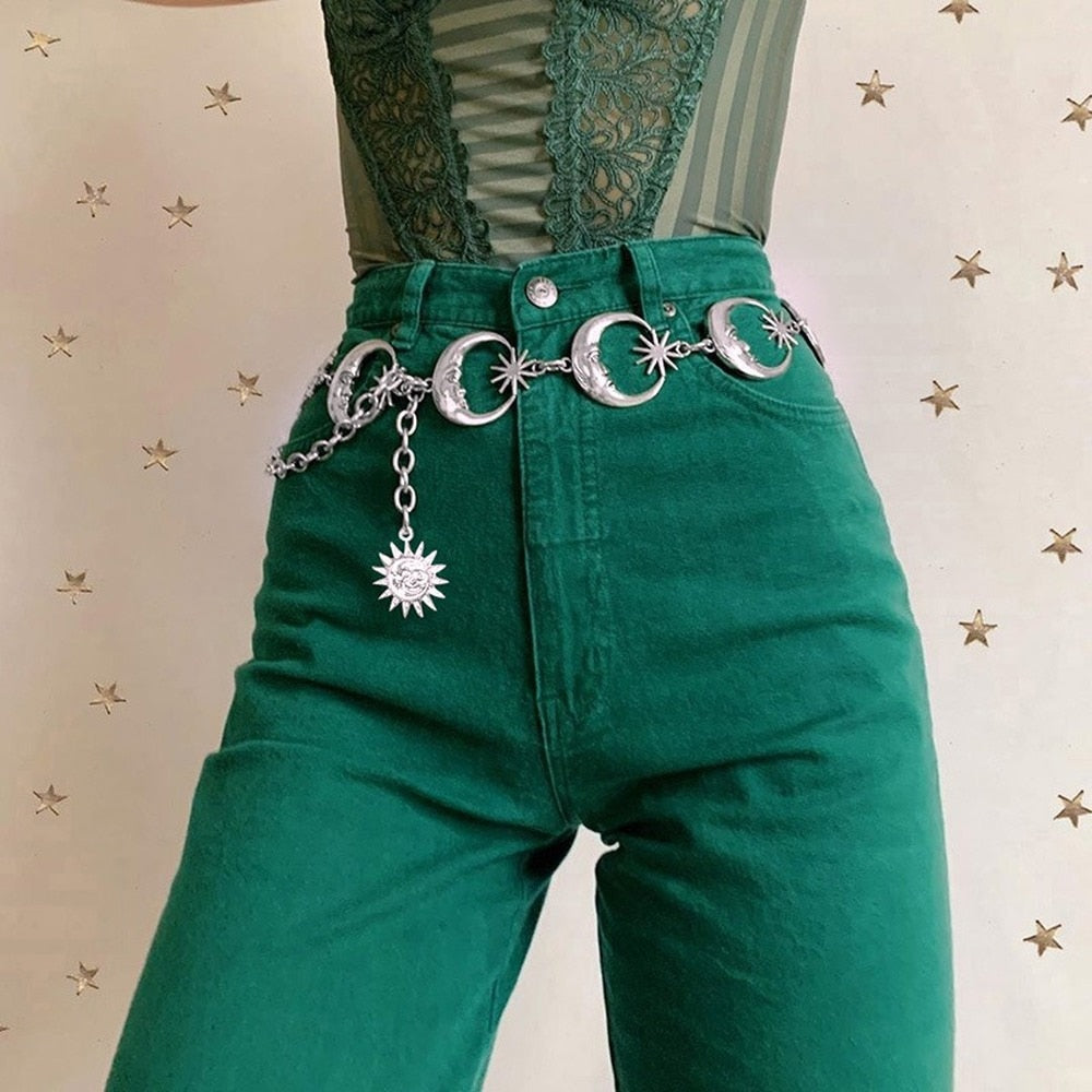 Front view of the celestial chain belt against green trousers, with moon faces linked across the waist and a draped side chain.