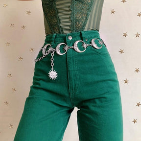 Front view of the celestial chain belt against green trousers, with moon faces linked across the waist and a draped side chain.