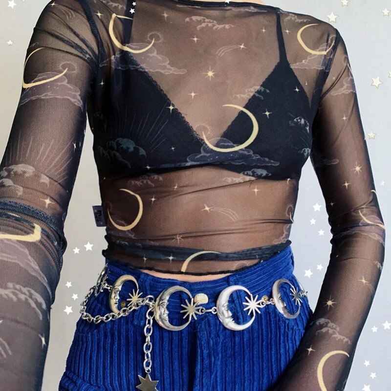 Silver crescent moon chain belt styled with blue corduroy trousers and a sheer wrap-front celestial top against a star-decorated wall.
