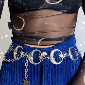 Close waist-level view of silver-tone moon faces and pointed stars linked across blue trousers, with a dangling charm below.