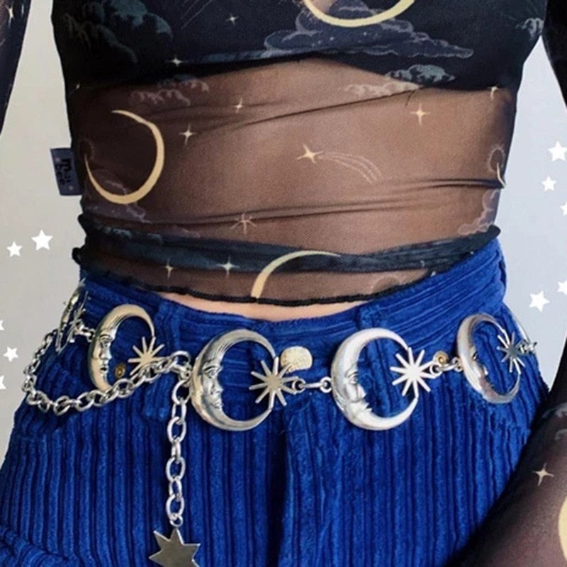 Close waist-level view of silver-tone moon faces and pointed stars linked across blue trousers, with a dangling charm below.
