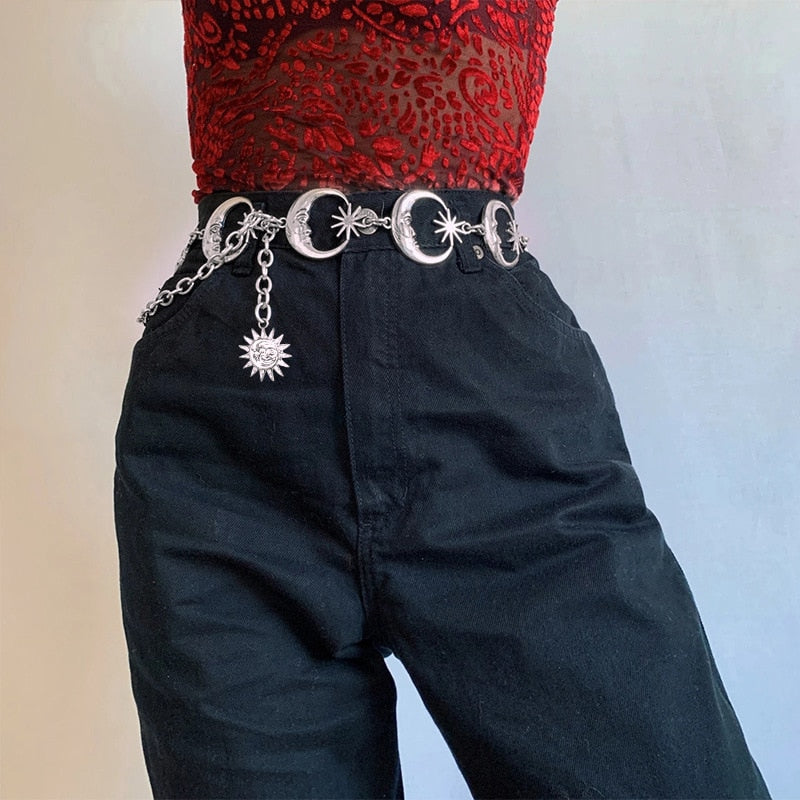 Silver-tone celestial chain belt around black high-waisted trousers, with a red brocade-style top visible above.