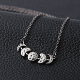Silver-tone moon phase necklace displayed against a dark textured background.