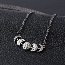 Silver-tone moon phase necklace displayed against a dark textured background.