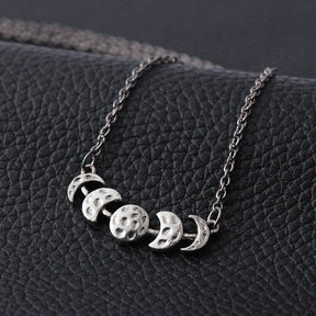 Silver-tone moon phase necklace displayed against a dark textured background.