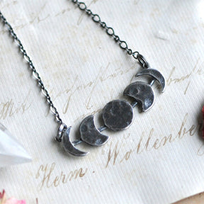 Silver-tone moon phase necklace showing its smooth reverse on a display card.