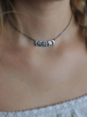 Silver-tone moon phase necklace worn at the neck with the lunar centerpiece visible.