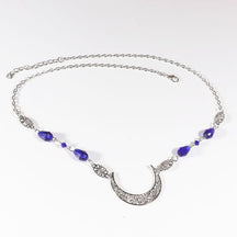 Silver-tone crescent head chain with large purple teardrop beads and small purple accents, arranged in an oval on a pale background with the clasp and chain visible.