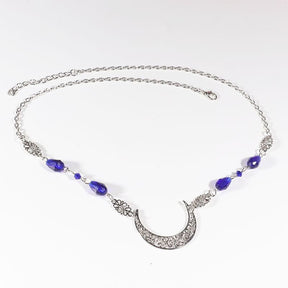 Silver-tone crescent head chain with large purple teardrop beads and small purple accents, arranged in an oval on a pale background with the clasp and chain visible.