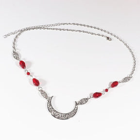 Silver-tone ornate crescent headdress with large red teardrop beads and smaller red accents, arranged in an oval on a pale background with the clasp and chain visible.