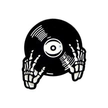 Black vinyl-record enamel pin held by illustrated white skeleton hands, with curved groove marks and a white circular centre label.
