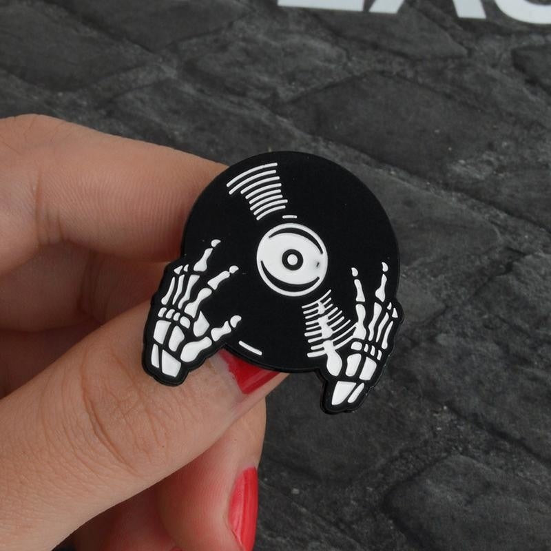 Record-hands pin held between fingers against gray fabric, showing the bony hands, white groove marks and circular record label.