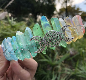 Angled view of a soft rainbow crystal point crown with a silver-tone triple moon emblem and wire-wrapped band.