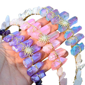 Purple, pink and iridescent crystal sun tiaras grouped on white, showing gold-tone emblems and pointed crystal crowns.