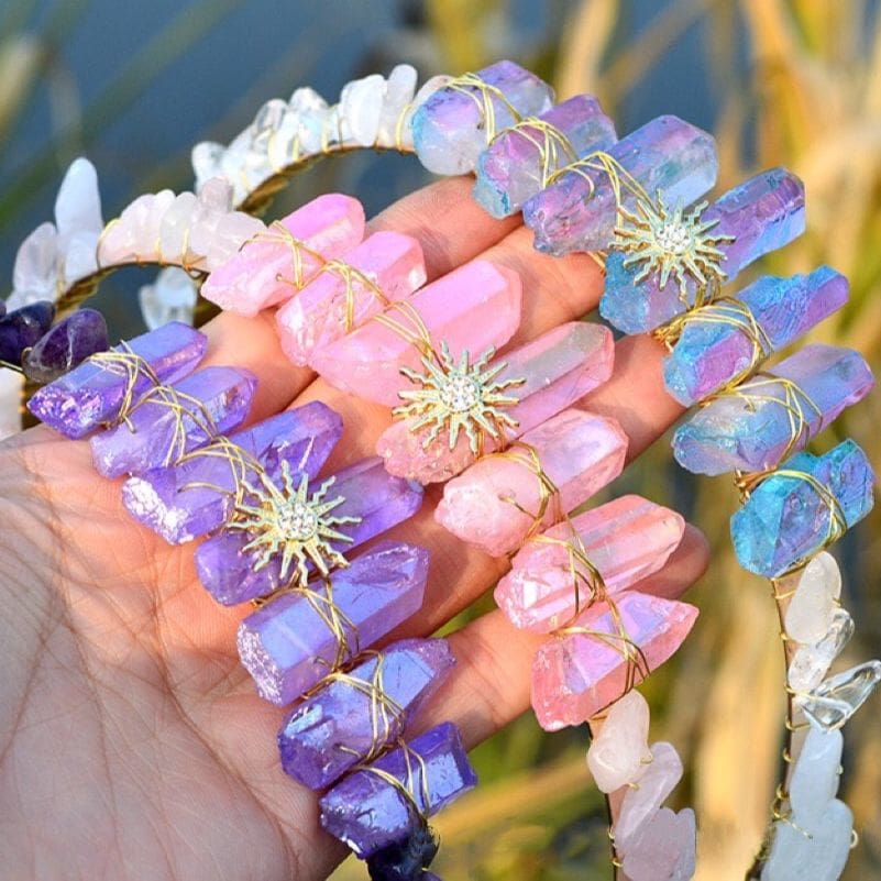 Purple, pink and iridescent sun tiaras displayed outdoors, with their tall points and gold-tone emblems visible together.
