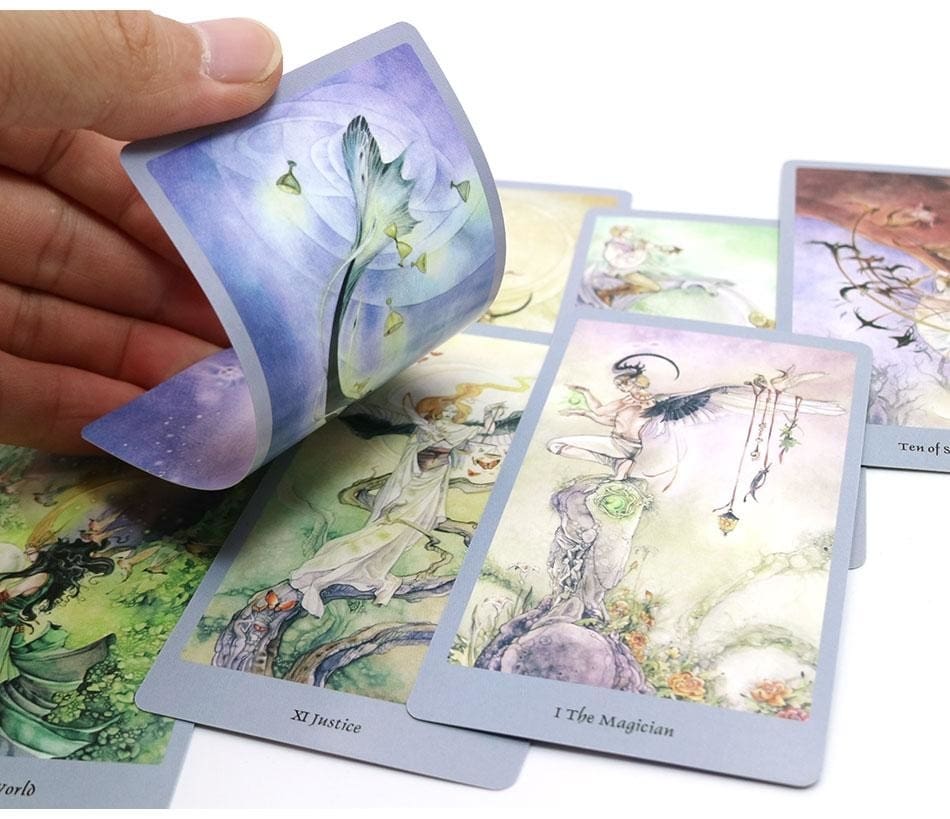 A tarot card gently bent in a hand above a spread of illustrated cards, showing the card surface and edge.
