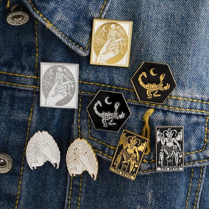 Tarot card and scorpion pins arranged on blue denim, showing a mixture of rectangular cards and curved animal silhouettes.
