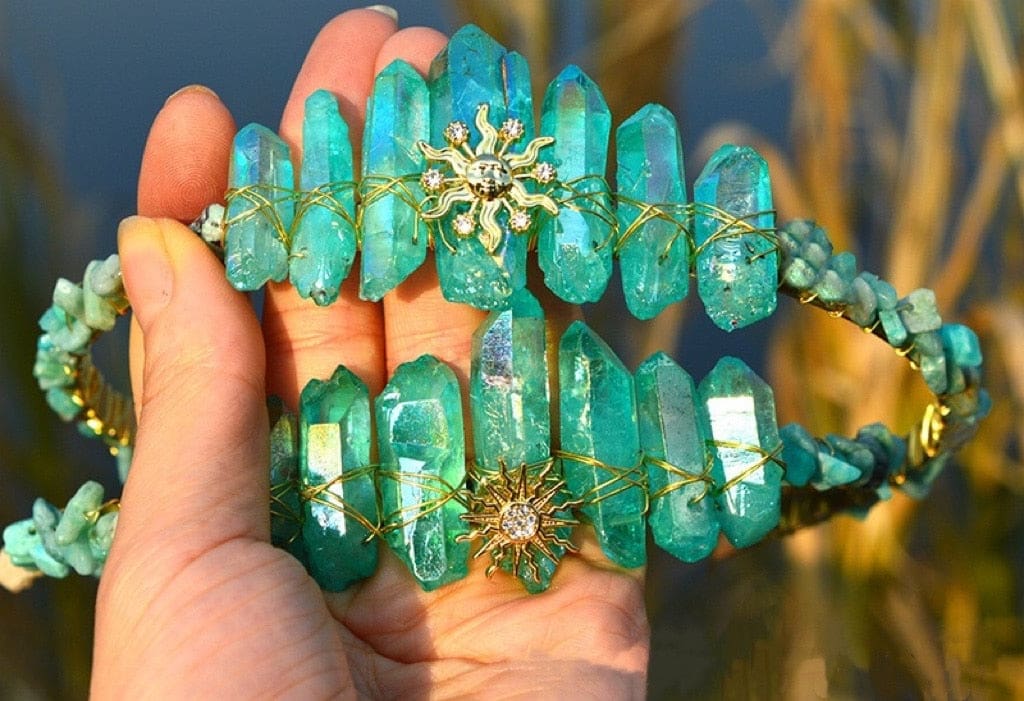 Two teal crystal tiaras held together, comparing the gold-tone Sun Face and Sunburst centre designs.