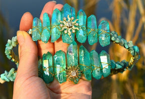 Two teal crystal tiaras held together, comparing the gold-tone Sun Face and Sunburst centre designs.