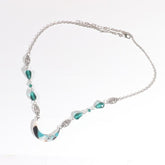Silver-tone chain headdress with teal teardrop beads and a teal-and-white marbled acrylic crescent, arranged in an oval on a pale background with the clasp and chain visible.