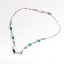 Silver-tone chain headdress with teal teardrop beads and a teal-and-white marbled acrylic crescent, arranged in an oval on a pale background with the clasp and chain visible.