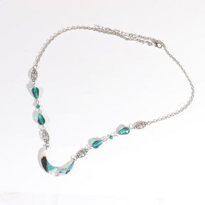 Silver-tone chain headdress with teal teardrop beads and a teal-and-white marbled acrylic crescent, arranged in an oval on a pale background with the clasp and chain visible.
