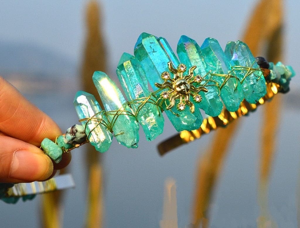 Teal crystal tiara with a gold-tone sun face and tall blue-green points forming the crown outline.
