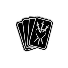 Black tarot-card enamel pin showing three overlapping cards, with a heart pierced by three swords on the front card.