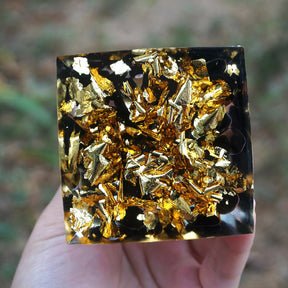 Tiger eye and obsidian orgone pyramid with a golden-brown sphere and blue Tree of Life inlay. Underside view of the dark obsidian pieces mixed with bright metallic flecks.