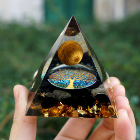 Additional view of Tiger eye and obsidian orgone pyramid with a golden-brown sphere and blue Tree of Life inlay. A full front view held farther from the camera shows the pointed outline and tree inlay.