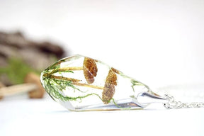 Horizontal side view of the faceted woodland pendant, with brown mushroom caps and green strands visible through the clear angular edges.