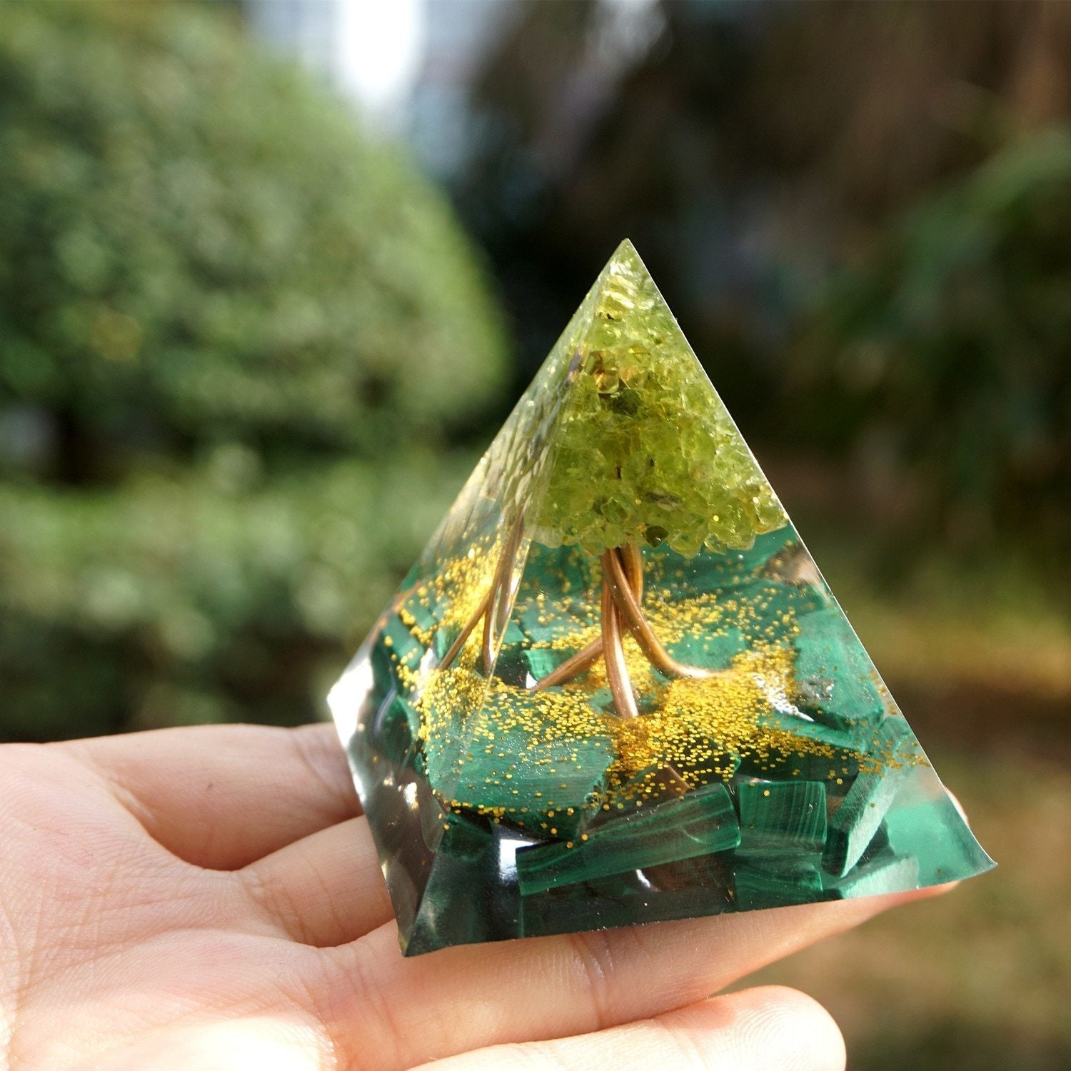 Tree of Life pyramid angled on a palm, showing the fine branches and green canopy above the malachite base.