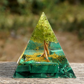 Full view of the clear Tree of Life pyramid on a wooden surface, showing green stones around the warm metallic tree.