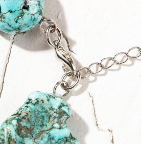 Close-up of the choker's silver-tone lobster-claw clasp and extension chain beside turquoise-coloured beads.
