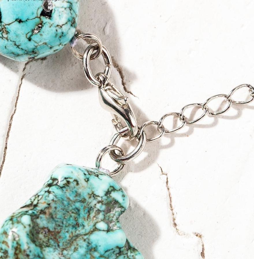 Close-up of the choker's silver-tone lobster-claw clasp and extension chain beside turquoise-coloured beads.