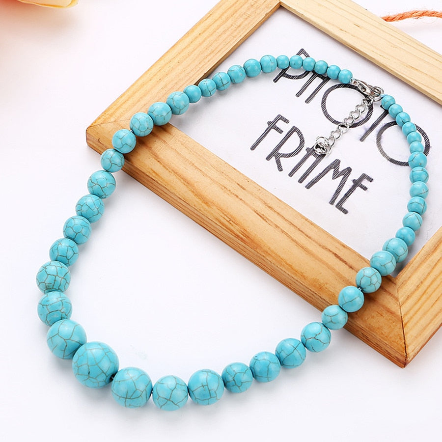 Turquoise-coloured round-bead necklace arranged beside a frame, with the graduated bead pattern facing forward.