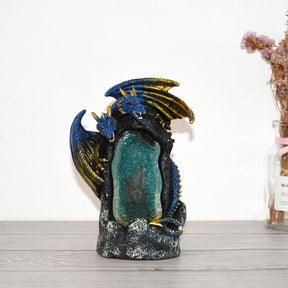 Twin blue dragons curve around the crystal-style cave burner on a pale tabletop, with a small plant arrangement beside it.