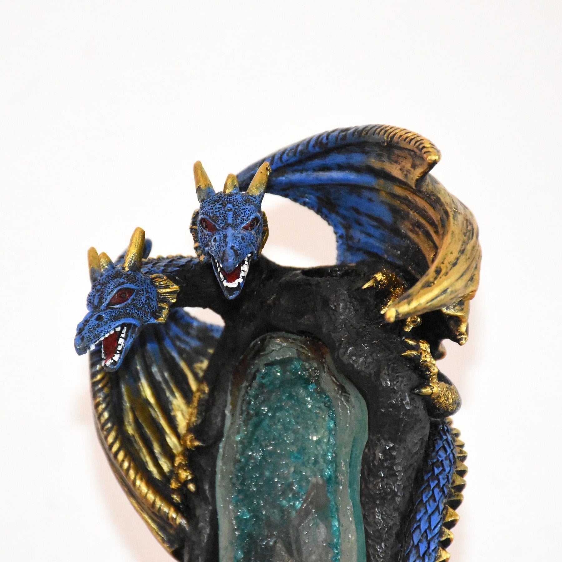 Close-up of the two dragon heads above the cave opening, with gold-tone horns and raised wings framing the blue scales.