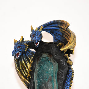 Close-up of the two dragon heads above the cave opening, with gold-tone horns and raised wings framing the blue scales.