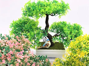 Closer view of colourful artificial bonsai foliage and branching trunks in a grouped display of white pots.