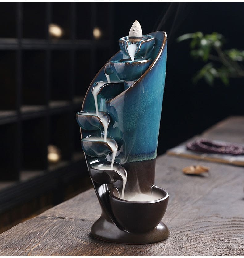 Angled view of the blue backflow incense burner, showing the depth of the curved bowls and the smoke path down the front.