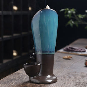 Back view of the blue waterfall incense burner, showing the tall glazed surface and dark base on a wooden tabletop.