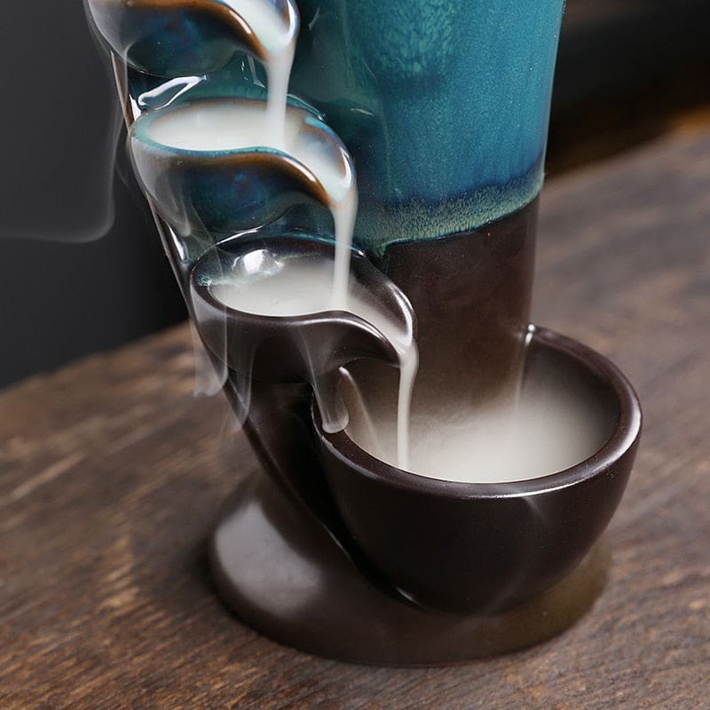 Lower section of the blue and brown waterfall burner, showing smoke passing through small bowls into the large dark base basin.
