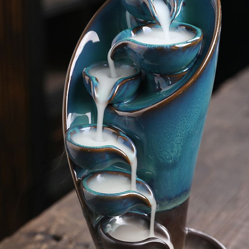 Close-up of the glossy blue burner's upper bowls, with a white stream of incense smoke spilling over their lips.